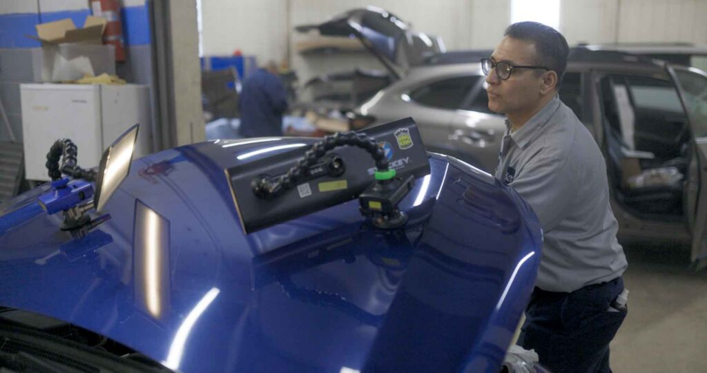 Zamora’s Auto Body Rockville MD-44 Technician inspecting dents on a blue car during collision repair service